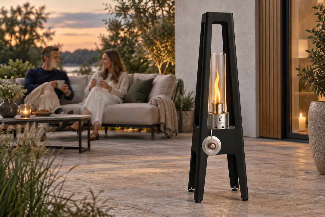 TORRE Black bioethanol lamp with metal legs in the foreground of an outdoor seating area with people farther behind.