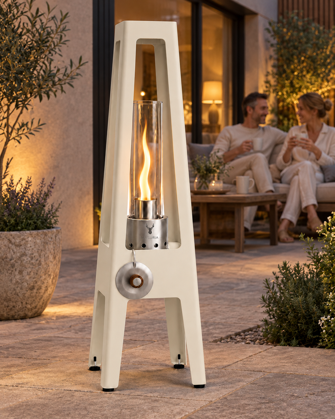 Lampe au bioéthanol TORRE Ivory Frost au premier plan d'un espace de détente extérieur ; les personnes sont assises plus loin.